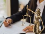 Justice statue and person in suit writing on paperwork